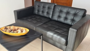Ein schwarzes Ledersofa mit einer gelben Schüssel auf einem schwarzen Tisch in einem Raum mit Fliesenboden.