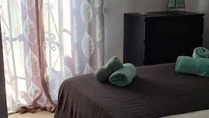 Ein Schlafzimmer mit einem Bett, einem Nachttisch, einem Spiegel und einem Fenster mit Vorhängen.
