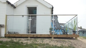 Een wit huis met een glazen veranda, een houten terras en een metalen trap naar een terras.
