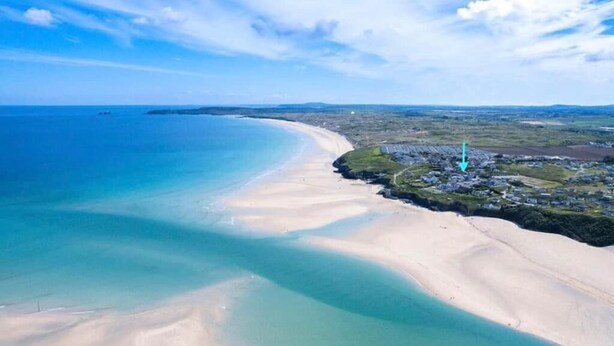 Luchtbeeld van een kustgebied met een zandstrand, een kleine nederzetting en een vuurtoren.