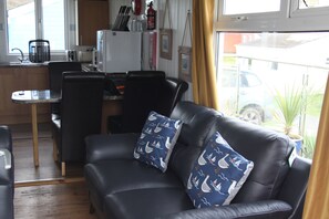 A living room with a black leather sofa, two patterned pillows, a small table, and a kitchen area in the background.