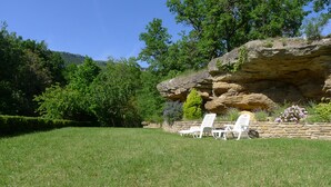 A grassy lawn with two white lounge chairs and a stone wall with a rock formation. - house / villa - Saint-PrivatHouse with garden (Saint-Privat)