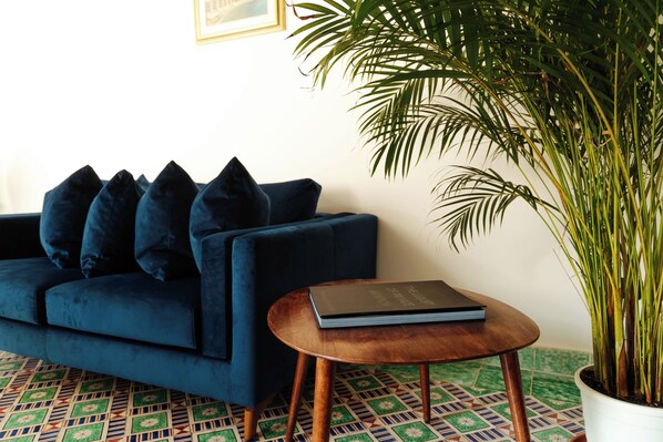 A blue sofa with dark cushions, a small wooden table with a book, and a potted plant. - Casa Lauritano (Atrani)