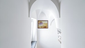 Ein Flur mit weißen Wänden und einer hohen, gewölbten Decke. Ein gerahmtes Gemälde ist an der Wand aufgehängt.