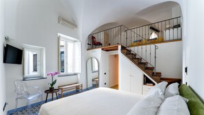 Ein Schlafzimmer mit einem großen Bett, einer Holztreppe, einem Sessel, einem kleinen Tisch und einem an der Wand befestigten Fernseher.