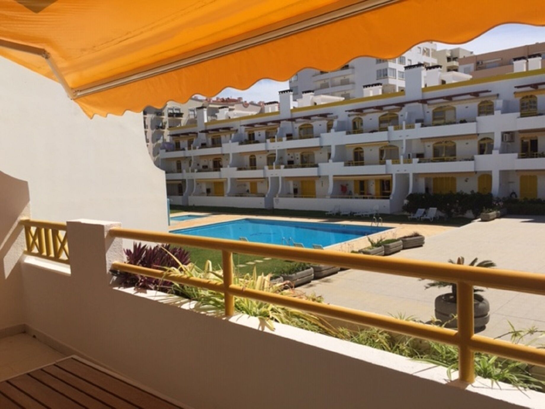 A hotel balcony with a view of a pool and a multi-story building with balconies.