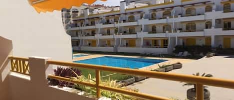 A hotel balcony with a view of a pool and a multi-story building with balconies.
