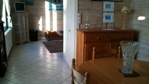 A dining area with a wooden table and chairs, a vase, and a lamp. There is a cabinet with a television on top and a framed picture on the wall.
