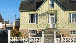 A two-story house with a green and beige exterior, a front porch, and a white picket fence.