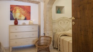 A bedroom with a bed, a wooden dresser, a wicker chair, and a painting on the wall. - Villa in Monopoli for 12 guests in six bedroom (Bari)