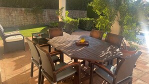 An outdoor patio with a wooden table and wicker chairs, surrounded by stone walls and greenery. - 3 bedrooms, 3 bathrooms, private heated pool, garden area and golf course views (San Roque)