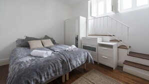 Un dormitorio con cama, cómoda, mesita de noche, ventana y escalera.
