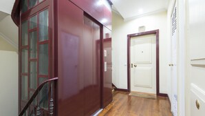Un pasillo con piso de madera, un ascensor rojo y una puerta blanca.