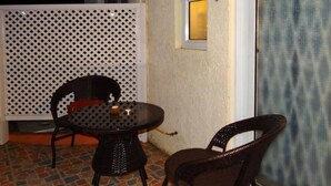 An outdoor seating area with two wicker chairs and a small round table, a white lattice partition, and a window with a view of the sky.