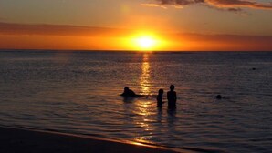 A sunset over a calm sea with silhouettes of people in the water.