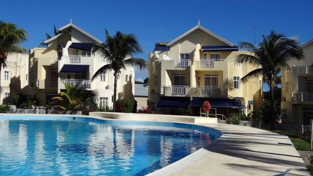 A swimming pool with lounge chairs, palm trees, and multi-story buildings with balconies.