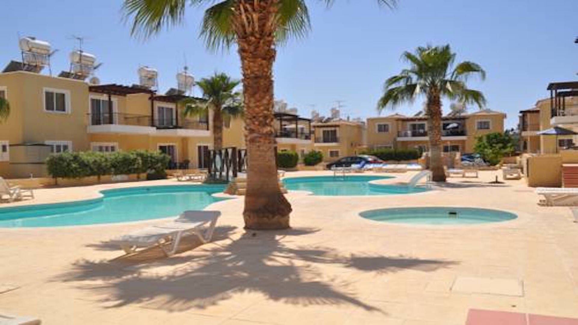 A pool area with multiple swimming pools, palm trees, and a building with balconies.
