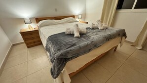 A neatly made bed with a grey blanket, two bedside lamps, and a wooden nightstand. -  2 Bedroom Apartment, Sirena Sunrise, Paphos (Paphos)