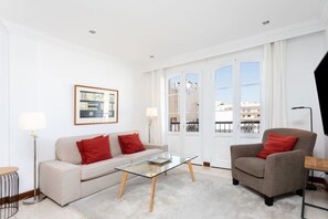 A modern living room with a sofa, armchair, glass coffee table, and a framed picture on the wall.