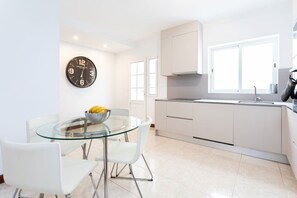 A modern kitchen with white cabinets, a glass dining table, and a clock on the wall.