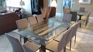 Een moderne eetruimte met een tafel met glazen blad en stoelen met kussens.
