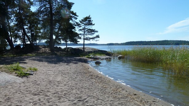 A sandy beach with a calm lake, surrounded by trees and rocks. - Unique Countryside Villa From The 17th Century, Close To Stockholm (Drottningholm)