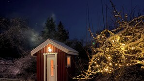 A small wooden cabin with a single door and a light on the front, surrounded by snow-covered ground and trees. - Unique Countryside Villa From The 17th Century, Close To Stockholm (Drottningholm)