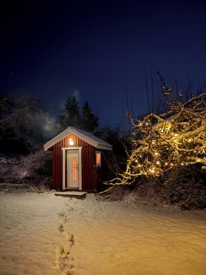 A small wooden cabin with a single door and a light on the front, surrounded by snow-covered ground and trees. - Unique Countryside Villa From The 17th Century, Close To Stockholm (Drottningholm)
