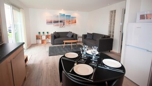 A modern living space with a dining area set for four, a sofa, and a refrigerator. - Coastal Apartments - Wales (Ground Floor) (Llanelli)