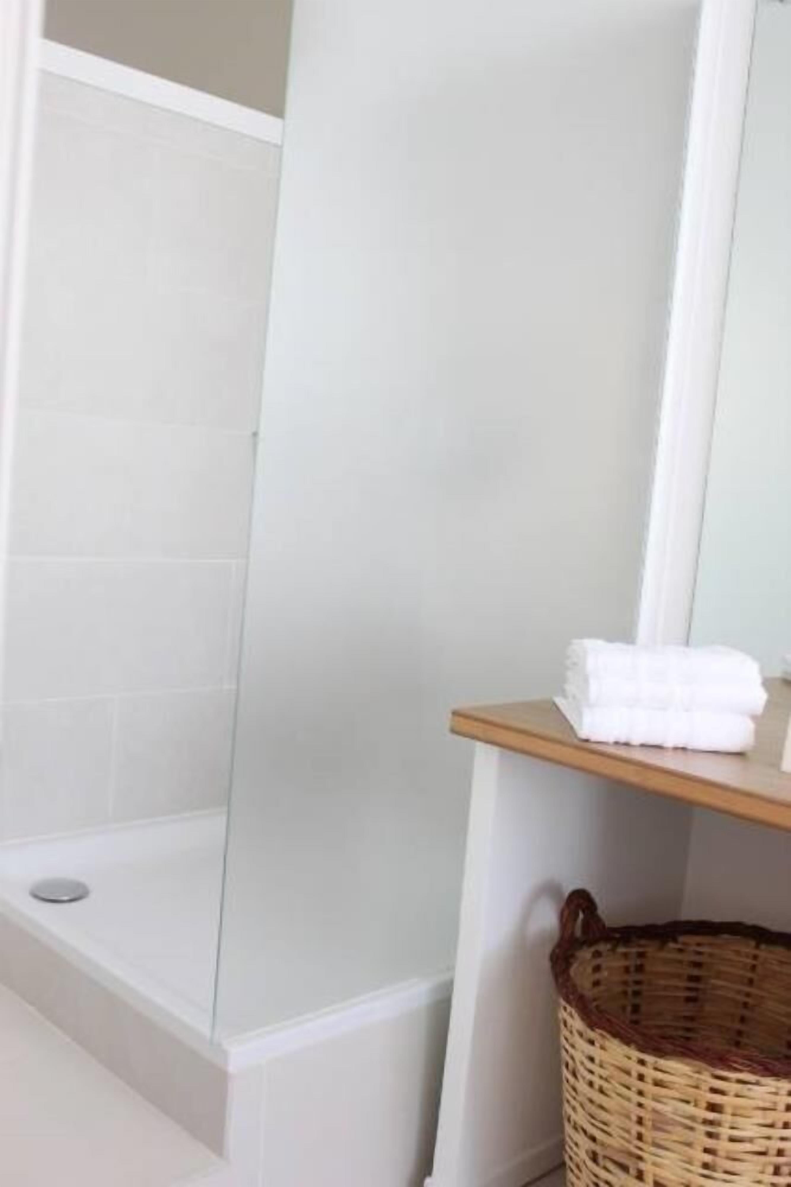 Une salle de bain avec une douche à parois de verre, une étagère en bois où sont pliés des serviettes et un panier en osier.