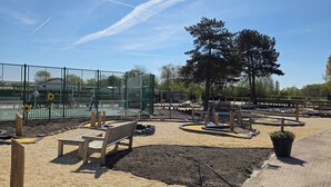 A fenced outdoor area with a basketball court, benches, and a dirt track.