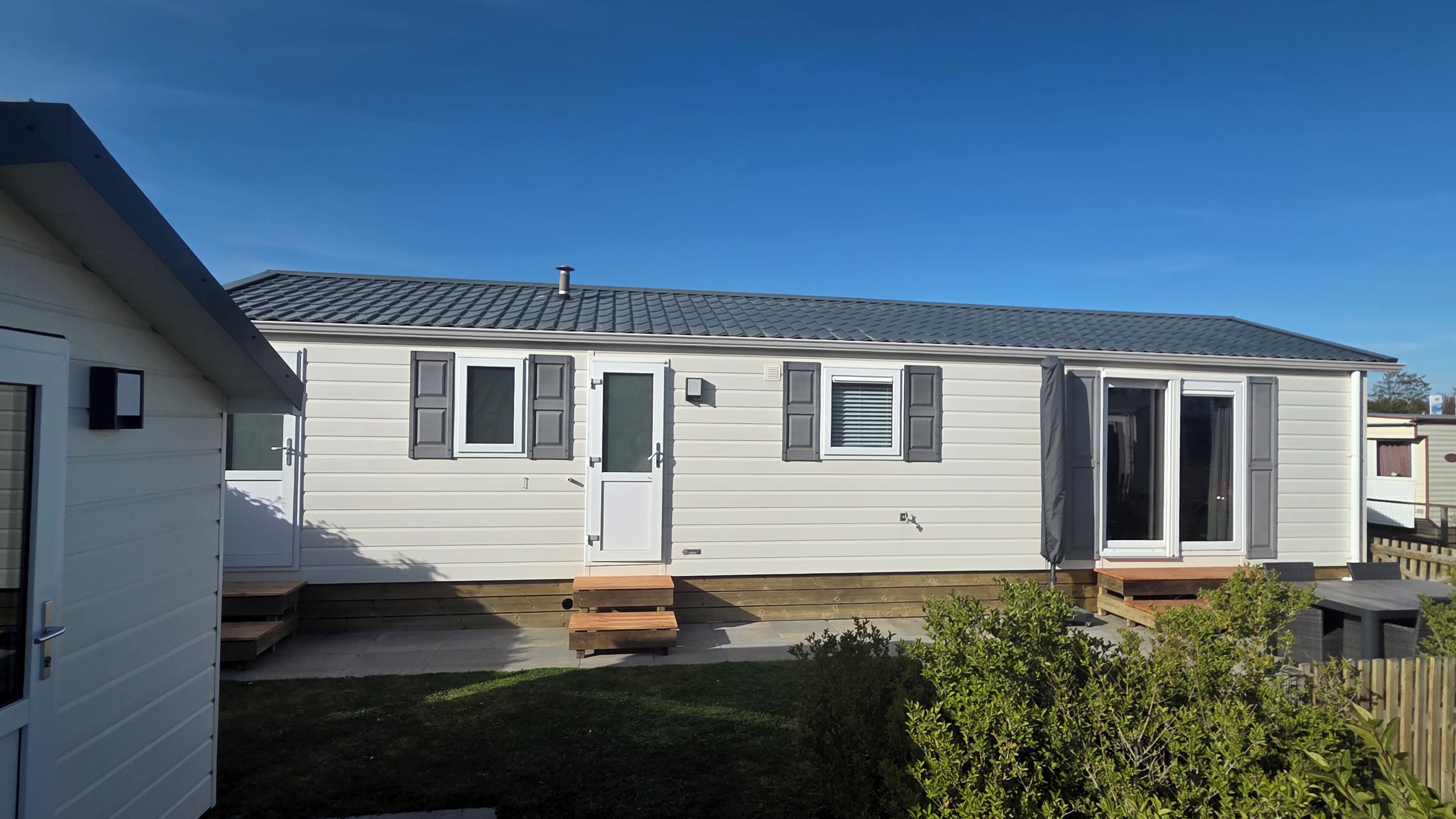 Une maison mobile de plain-pied avec une porte d’entrée, un petit porche et une terrasse couverte.