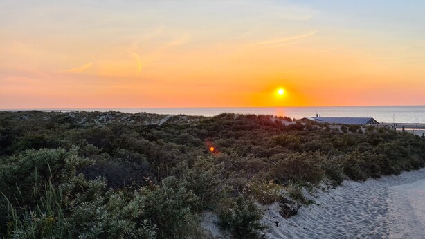 A beach with a dune system and a building with solar panels.