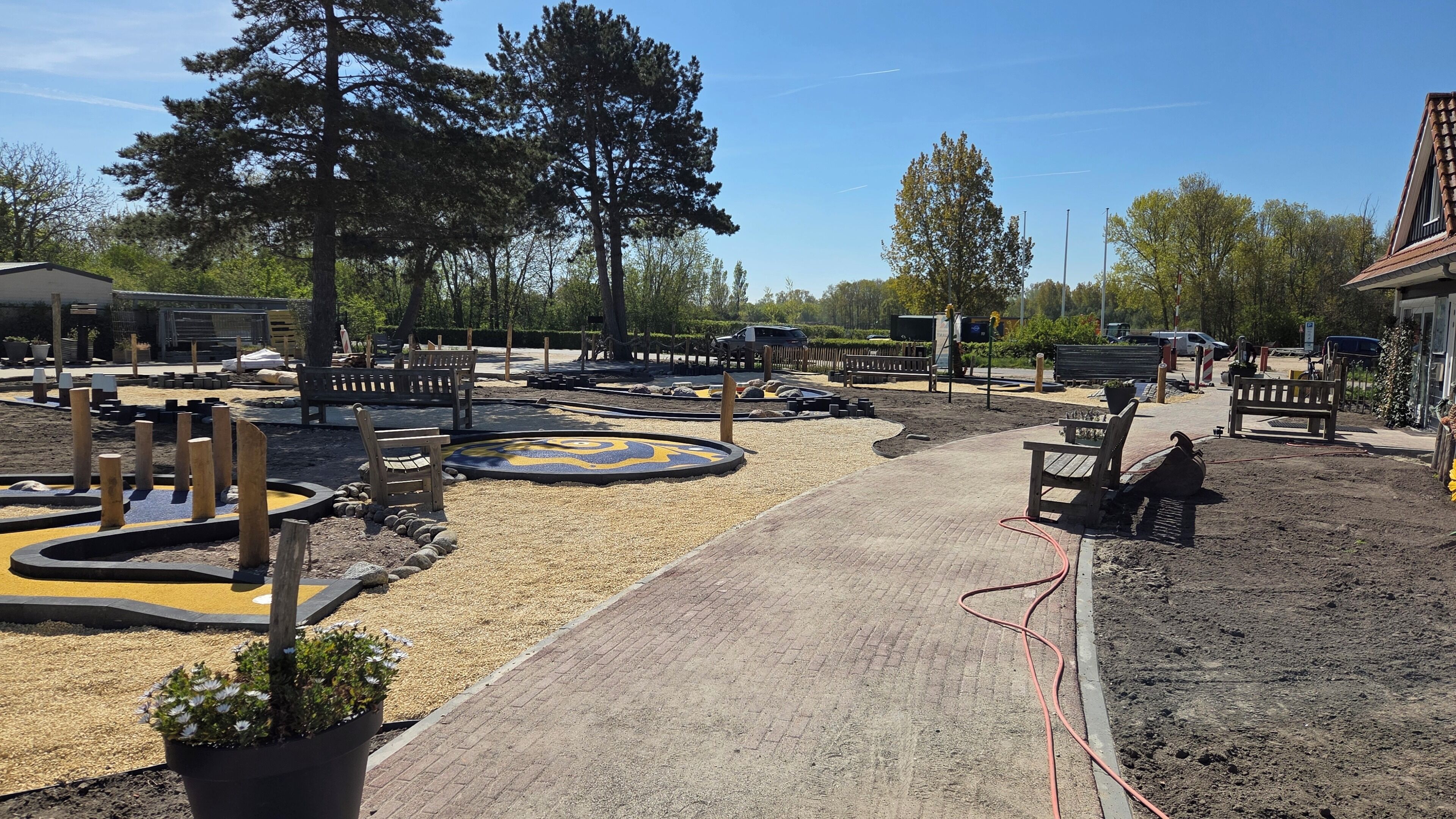 Un chemin pavé mène à un espace aménagé avec des bancs, entouré de gravier et de plantes en pot.