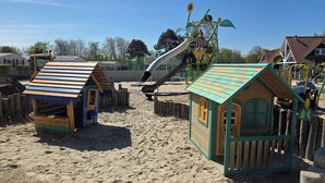 A sandy playground with wooden playhouses and a large slide.