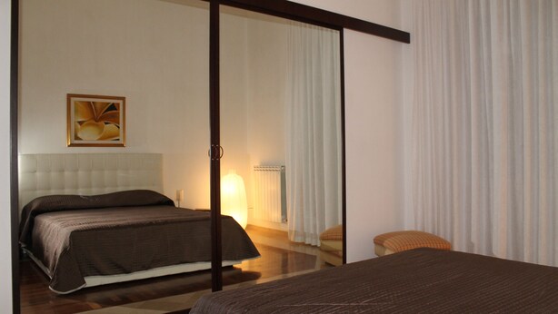 A hotel room with a large bed, a smaller bed, a chair, and a painting on the wall. - WONDER FLAT ORTIGIA: elegant flat (Siracusa)