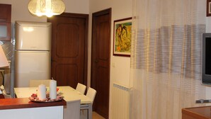 A kitchen with a refrigerator, wooden cabinets, a dining table with chairs, and a wall-mounted television. - WONDER FLAT ORTIGIA: elegant flat (Siracusa)