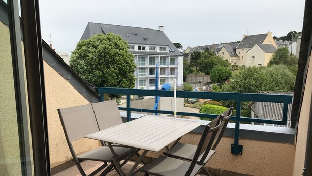 En balkon med et bord og stole, med udsigt over et boligområde med huse og grønt.