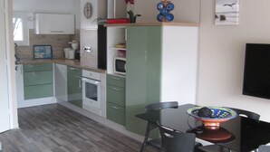 Et kompakt køkken med moderne hårde hvidevarer, et spiseområde med bord og stole, samt et fladskærms-tv monteret på væggen.
