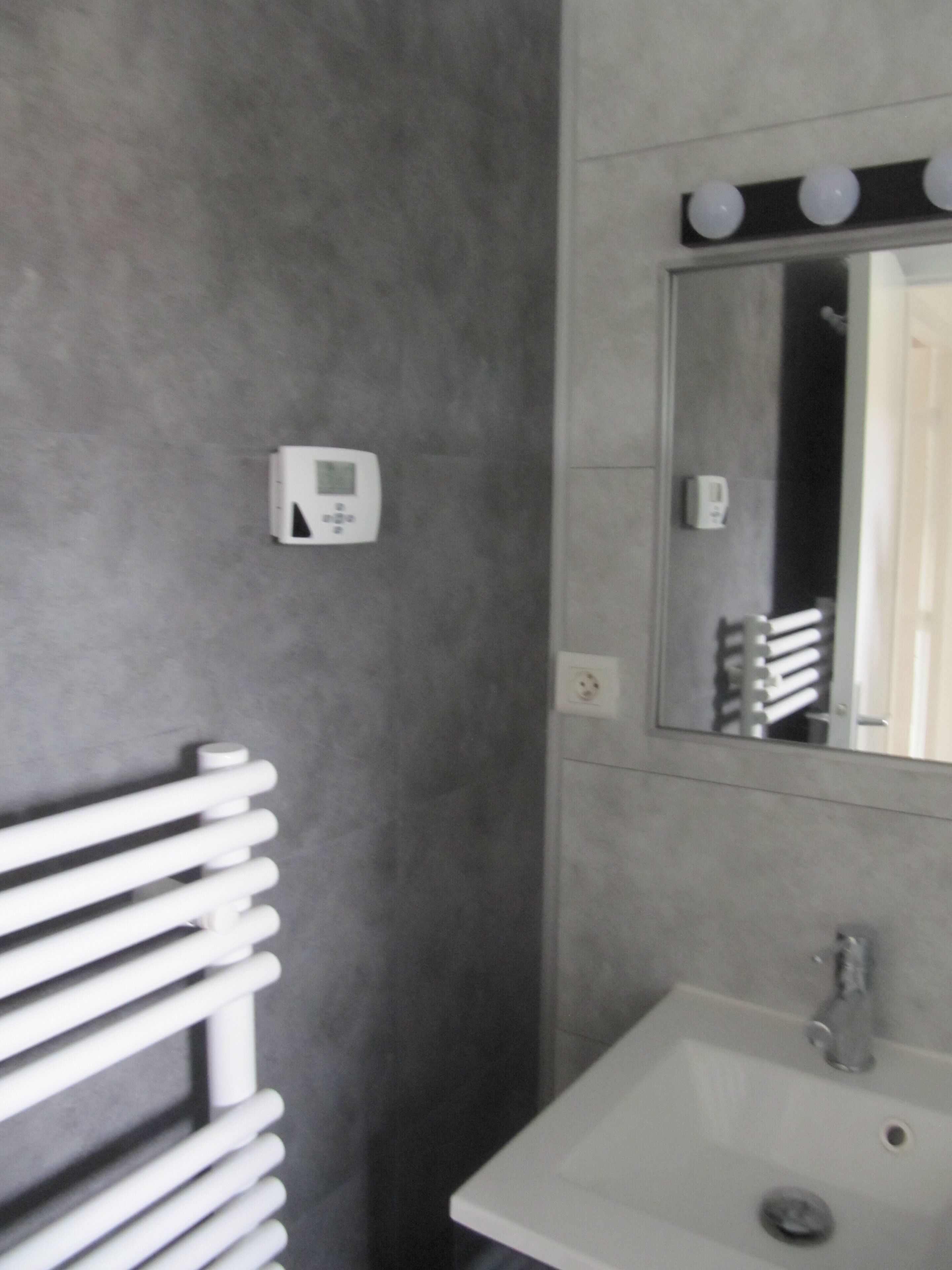 Un baño con lavamanos blanco, un espejo con iluminación y un perchero para toallas.