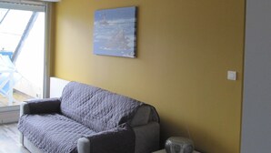 En stue med sofa, et lille natbord, en radio og et maleri på væggen.