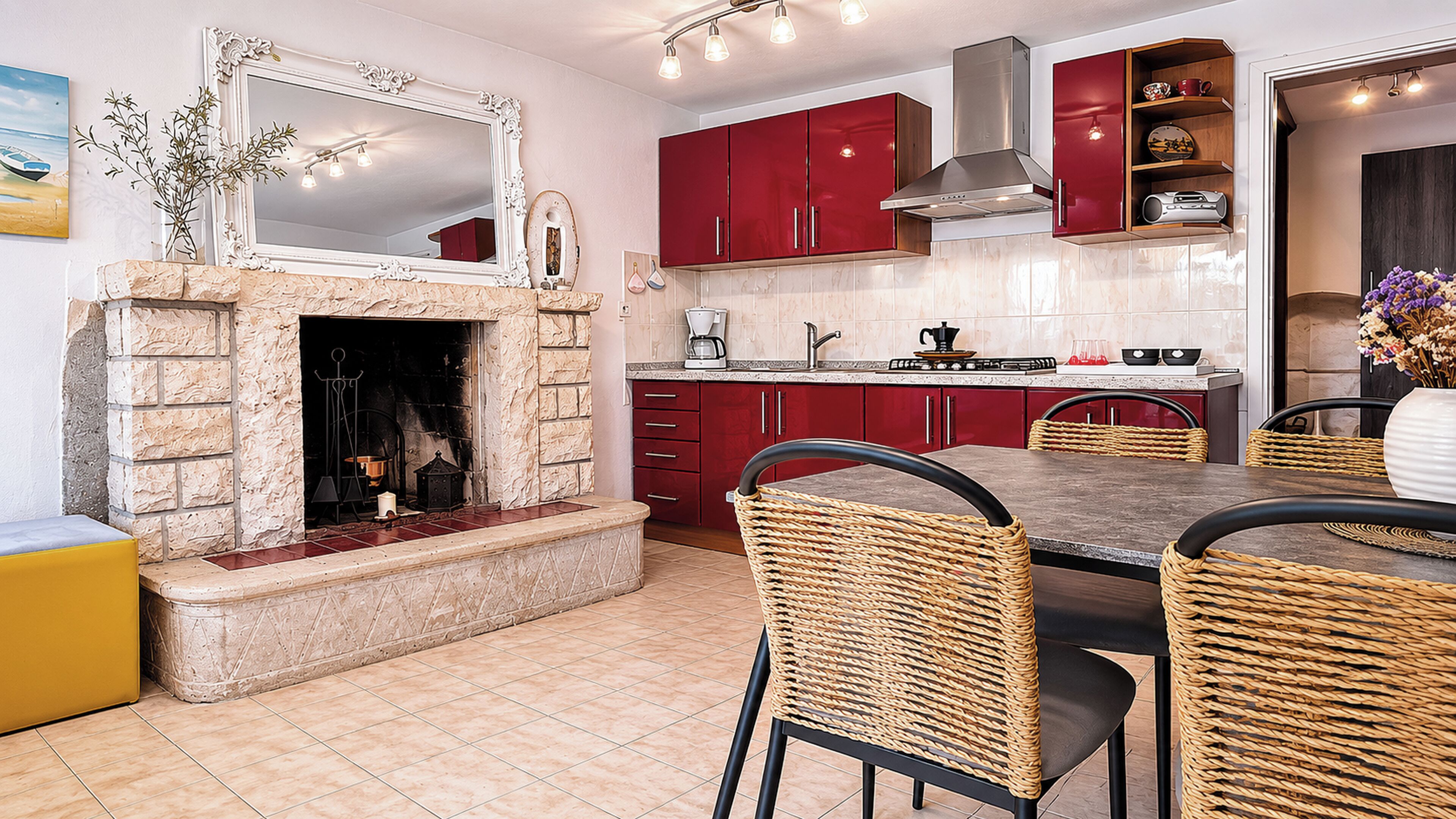A kitchen with red cabinets, a stone fireplace, and a dining area with wicker chairs.