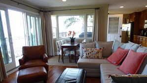 A living room with a leather armchair, a sofa with patterned cushions, a coffee table, and a dining area with a table and chairs.