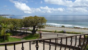 A balcony with a view of the ocean, a tree, and a paved walkway.