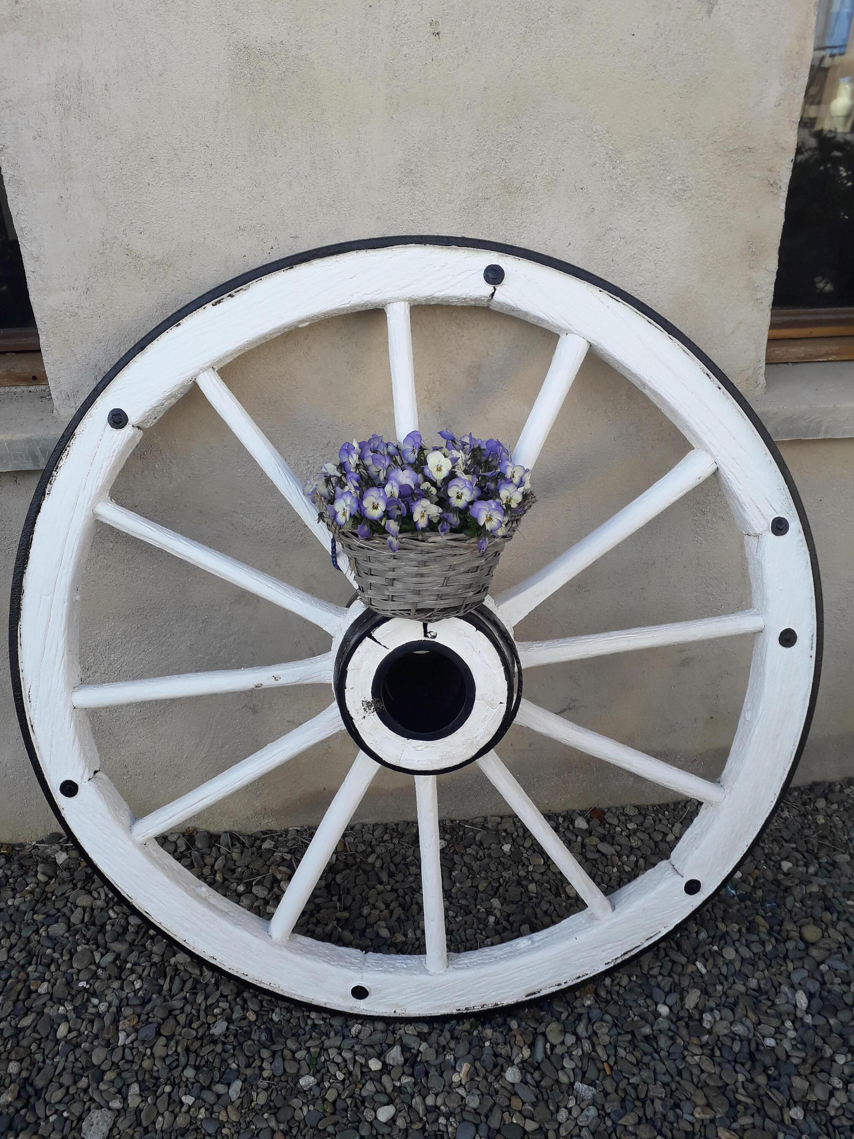 A white wooden wheel with a basket of flowers in the center, mounted on a concrete wall.