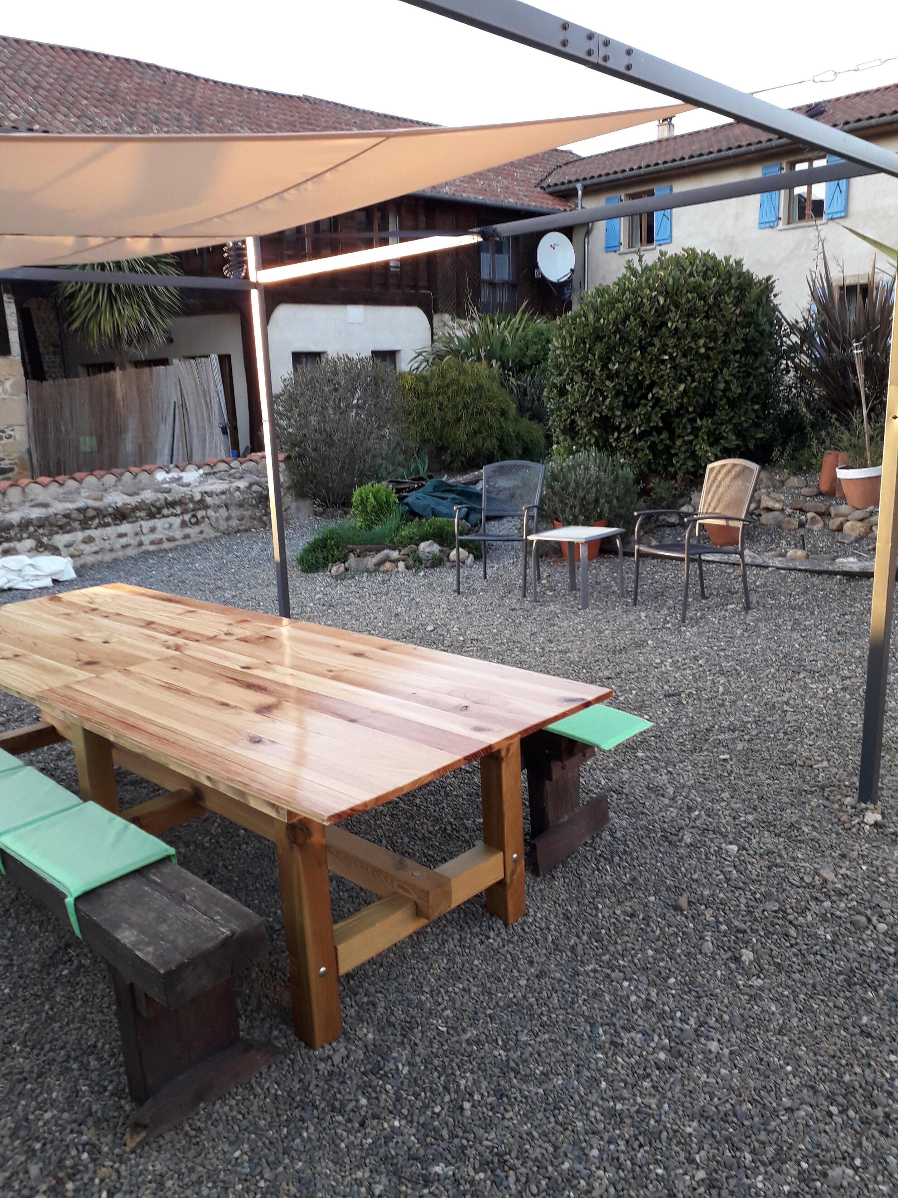 Eine Terrasse im Freien mit einem Holztisch und Bänken, umgeben von Kies und Topfpflanzen.