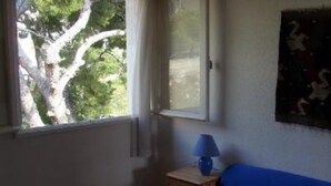 A bedroom with a bed, a window with a view of trees, a lamp on a bedside table, and a wall with a painting. - Apartment/ flat - Cassis (Cassis)