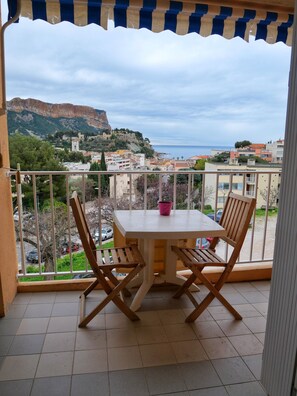 Un balcon avec une table et des chaises, donnant sur une ville côtière avec ses bâtiments et une montagne.