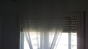 Une fenêtre avec des rideaux légers, un mur blanc et un chambranle de porte visible.