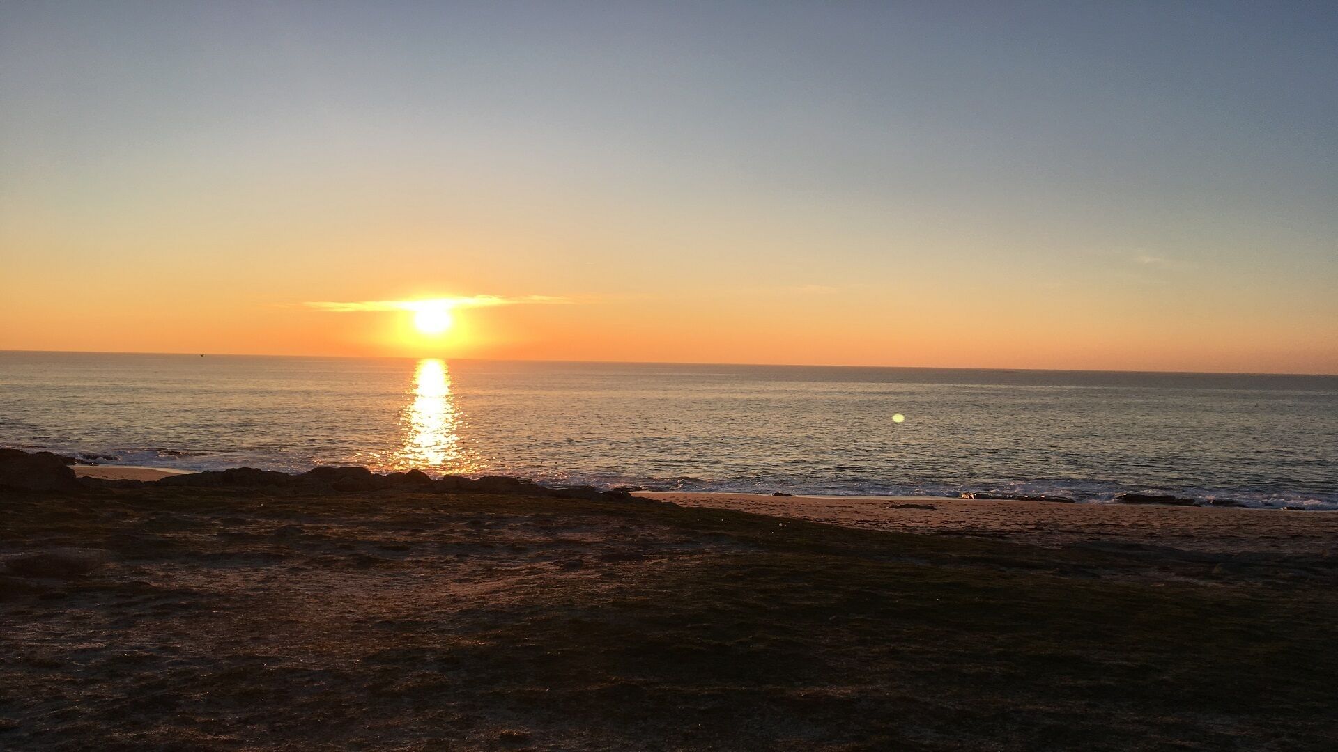 A sunset over the ocean with a beach in the foreground.
